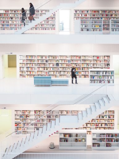 Library - Remarkable Reward - Helmut Oberritter Zwei Personen auf Treppen in einer modernen Bibliothek mit Regalen voller Bücher.