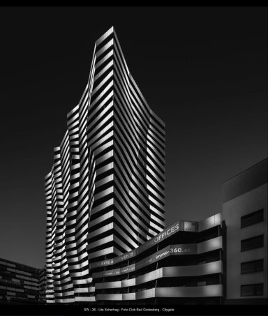 Ute Scherhag - SW 26 Moderne, gewundene Hochhausfassade in schwarz-weiß, gegen einen dunklen Himmel.