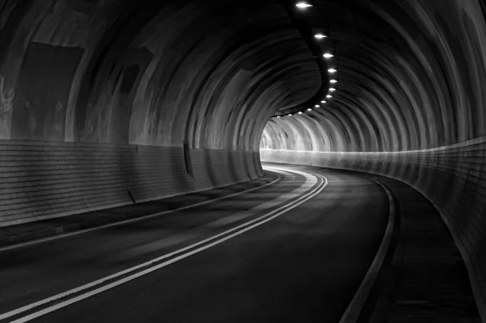 Februar 2026 - Uwe Müller Dunkler Tunnel mit geschwungener Fahrbahn und beleuchteten Wänden.