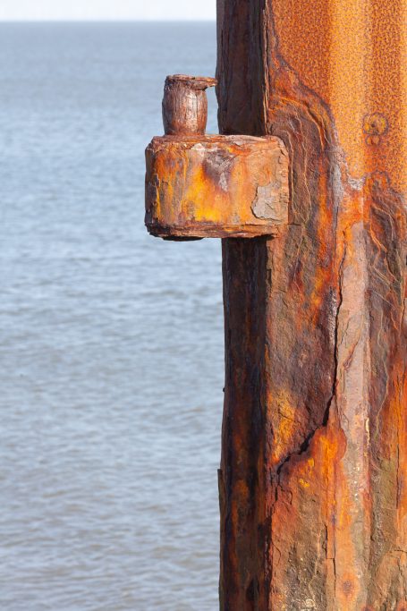Rost 02 Rostiger Metallbalken mit einer rauen Oberfläche, im Hintergrund Wasser.