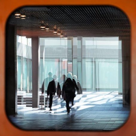 Spiegelung -3- Menschen gehen durch einen lichtdurchfluteten Gang mit modernen architektonischen Elementen.