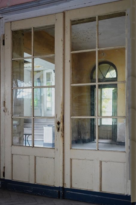 Hotel Bellevue -C- Holztür mit Glasscheiben, Blick in einen hellen Raum mit Fenster und Möbeln.
