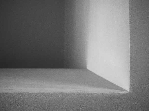 Licht und Schatten Graue Wand mit einem hellen Lichtstrahl, der eine Ecke beleuchtet.