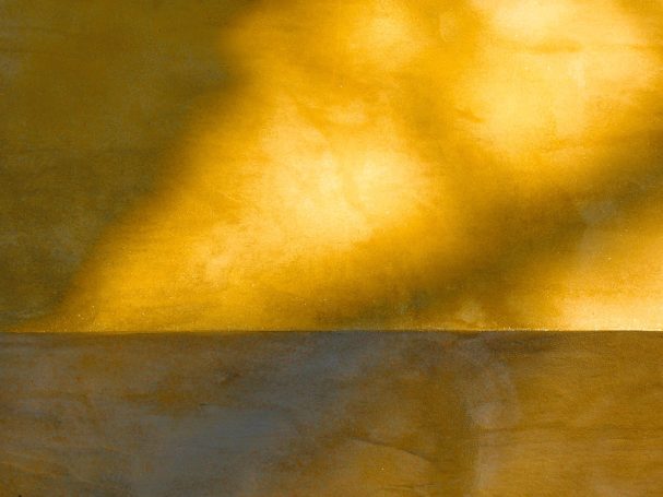 Abstrakt -1- Sonnenlicht wirft warme, gelbe Schatten auf eine strukturierte Wandoberfläche.