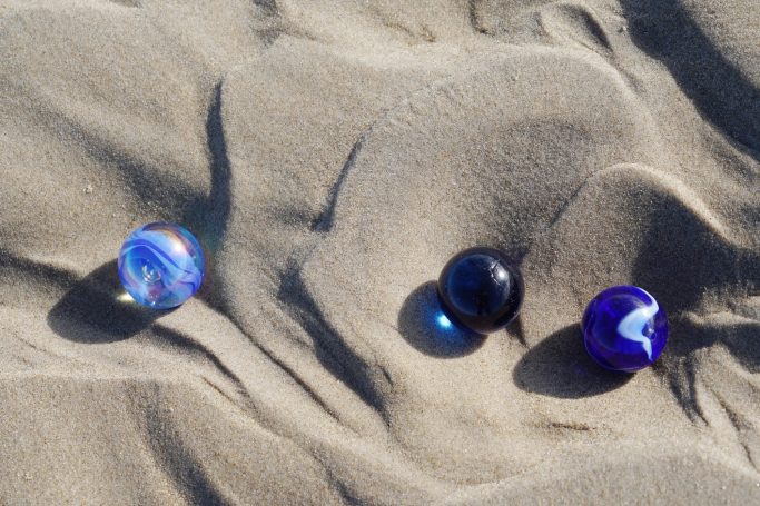 Sand -1- Drei Murmeln in verschiedenen Farben liegen auf sandiger Oberfläche.