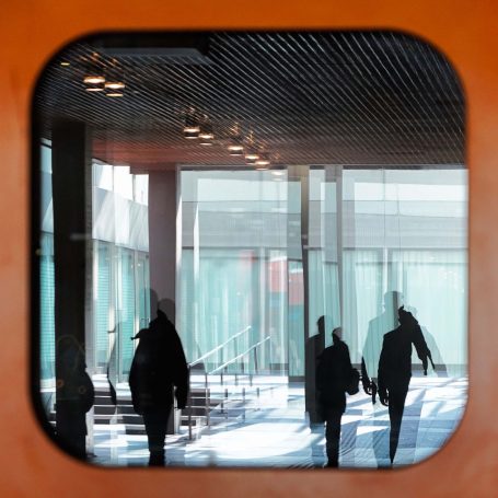 Januar 2025 - Kornelia Brinkmann-Roden Silhouetten von Menschen, die durch ein Fenster in einem modernen Gebäude gehen.