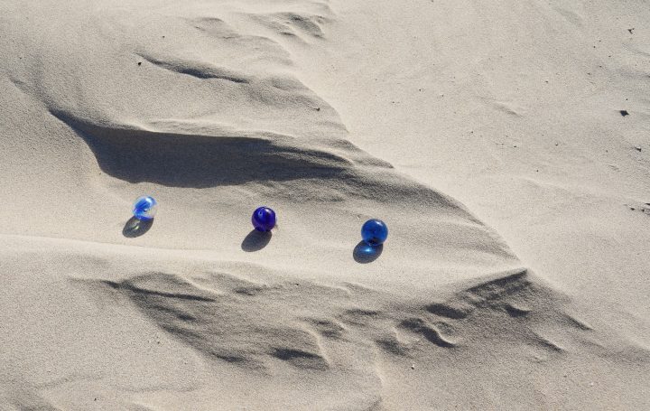 Sand -3- Drei bunte Murmeln liegen auf sanften Sanddünen.