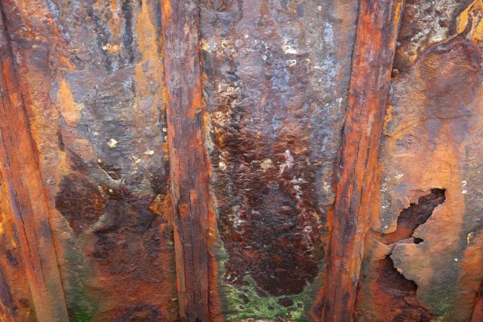 Rost 1ß Rostige Metalloberfläche mit braunen und grünen Flecken, teilweise beschädigt.